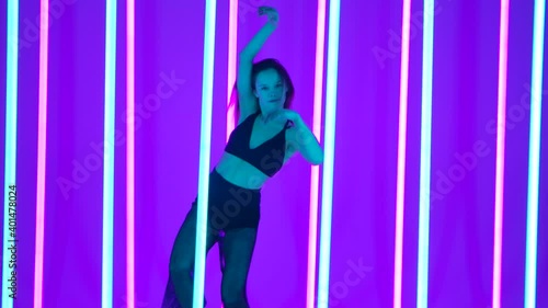 Wallpaper Mural A woman performs contemporary choreography in a studio illuminated by colorful neon tubes. The performer raises her arms in a sensual dance motion and grabs the neon pipes. Slow motion. Torontodigital.ca