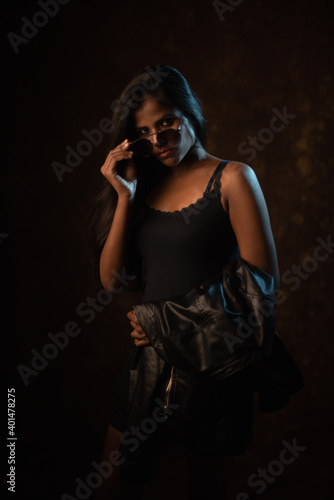 Fototapeta Studio portrait of a beautiful and young dark skinned Indian Bengali female model in black camisole and black leather jacket
