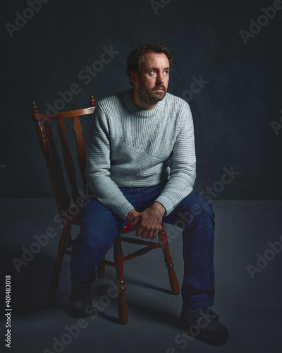 Young 40 year old Hispanic Caucasian man. Sitting in vintage chair with worried face, studio portrait. Well dressed, elegant and classic atmosphere.