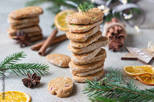 Stacked spicy butter cookies with candied fruits, cinnamon sticks and anise. Festive Christmas or New Year background with fir branches and dried oranges slices.