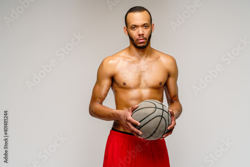 Muscular african american sportsman playing basketball shitless over light grey background photo