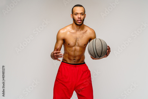 Muscular african american sportsman playing basketball shitless over light grey background