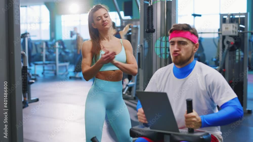 Caucasian funny man training on gym machine equipment having fun exercising making personal coach applauding. Fitness athlete woman. Workout team. Humor concept. Caucasian funny man training on gym machine equipment having fun exercising making personal coach applauding. Fitness athlete woman. Workout team. Humor concept.