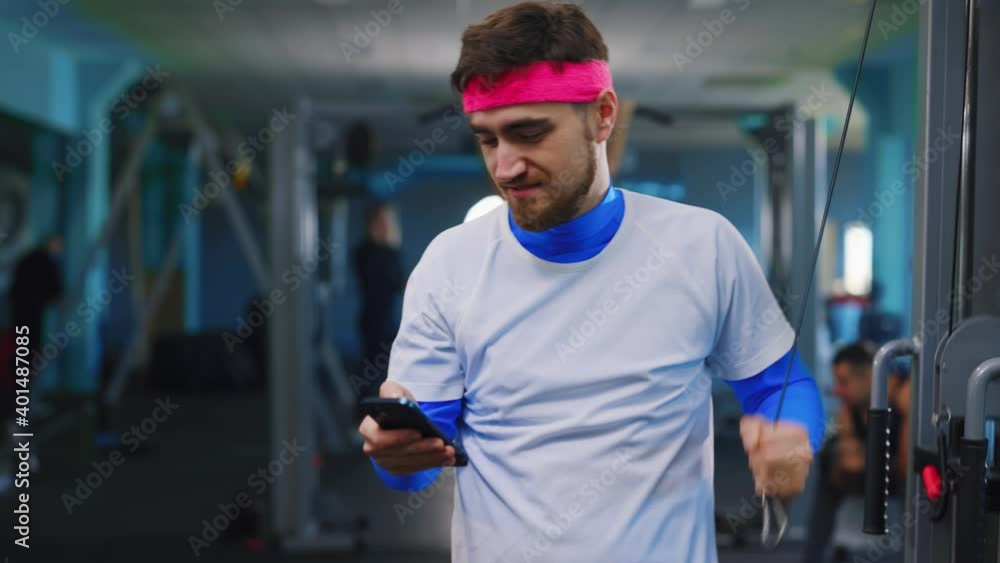 Funny bearded caucasian guy using smartphone while exercising lazy beginner training at the gym. Nomobphobia. Mobile phone addiction. Funny bearded caucasian guy using smartphone while exercising lazy beginner training at the gym. Nomobphobia. Mobile phone addiction.