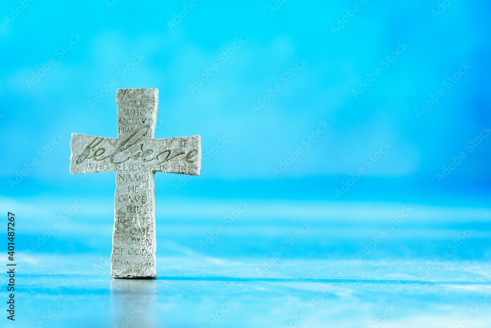 Stone cross with inscription Believe on blue background, Copy space. Christian backdrop. Biblical faith, gospel, salvation concept. Banner