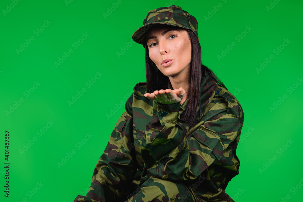 Awesome woman in military uniform blowing a kiss to the camera. Green background. Gender stereotype. Awesome woman in military uniform blowing a kiss to the camera. Green background. Gender stereotype.