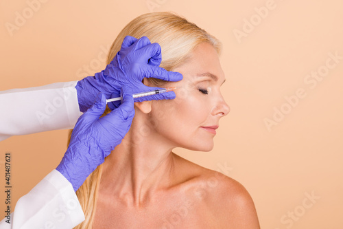 Profile photo middle aged woman try new plastic surgery injection her doctor make syringe gloves isolated beige color background