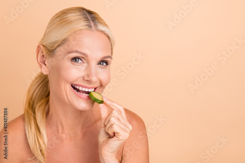 Close-up portrait of attractive blonde cheerful lady eating juicy cucumber healthy regime isolated over beige pastel color background