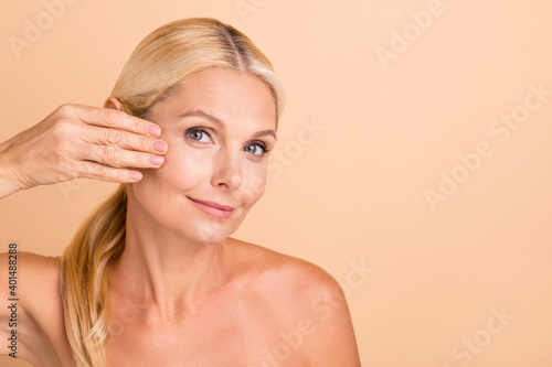Closeup photo of natural beauty aged lady nude shoulders touch fingers cheek apply anti age uplift cream isolated beige color background photo
