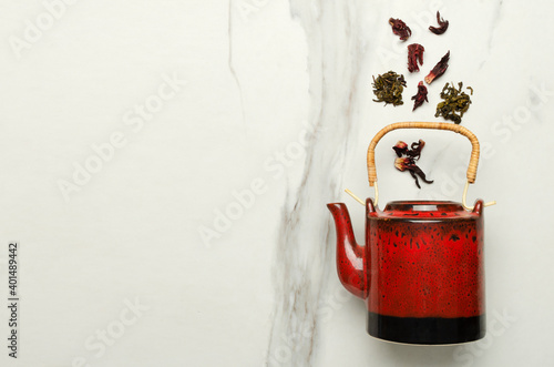 Red teapot and falling dried leaves of hibiscus and green tea on the marble table.Empty space