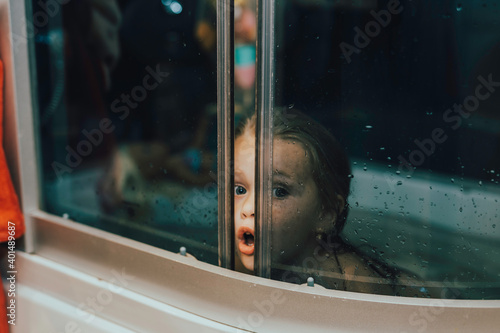 surprised nfocused girl is sitting in the bathtub and water drops on the glass of the shower stall