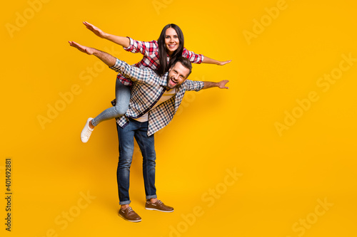Full length body size view of nice cheery couple piggy backing having fun dream vacation copy space isolated over bright yellow color background