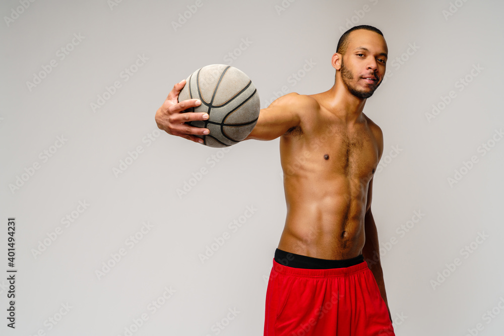 Muscular african american sportsman playing basketball shitless over light grey background