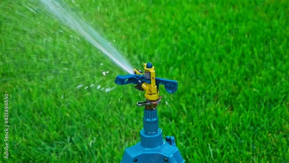 Head of Sprinkler on tripod watering grass of backyard Head of Sprinkler on tripod watering grass of backyard