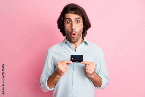 Portrait of young handsome shocked amazed man male guy with open mouth hold credit card wear glasses isolated on pink color background