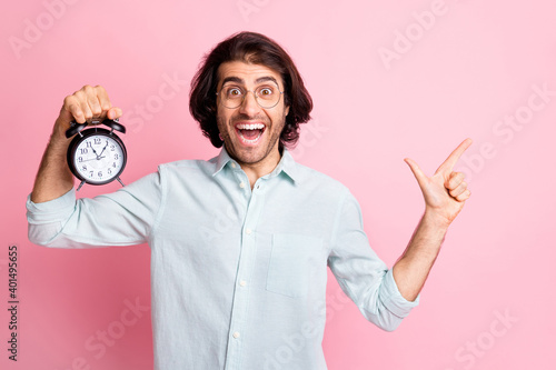 Photo of optimistic nice guy hold clock point empty space wear spectacles blue shirt isolated on pastel pink color background © deagreez