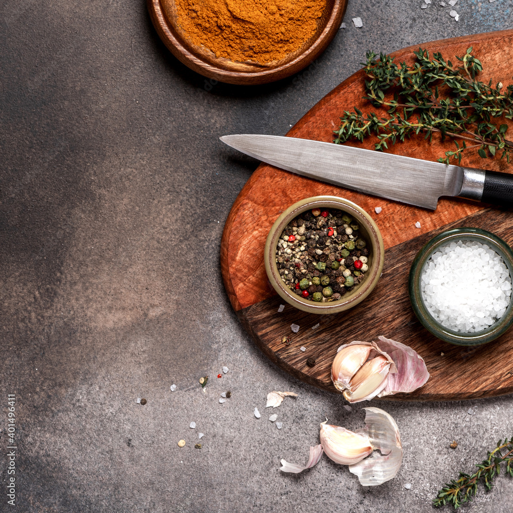 Food background. Various spices, thyme, knife, and a wooden cutting board on a black background top view. Copy space for text. Flat lay. Cooking food concept.