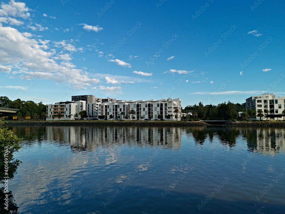 Fototapeta premium Beautiful view of a river with reflections of modern apartment buildings, blue sky and trees on water, Parramatta river, Wilson Park, Silverwater, Sydney, New South Wales, Australia 