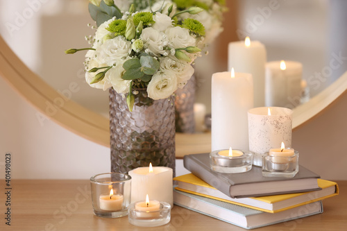 Beautiful burning candles  books and flowers on table at home
