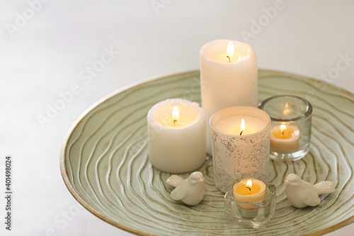 Beautiful burning candles on tray against light background