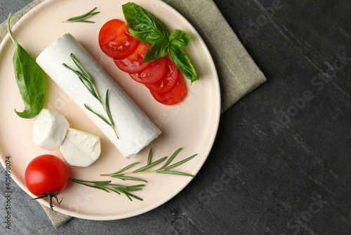 Delicious fresh goat cheese with tomatoes, basil and rosemary on grey table, flat lay