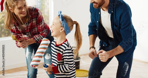 Close up of Caucasian happy family parents and little girl kid having fun, dancing and singing into roller brush together while renovating domestic room. Mom and dad playing with daughter. home repair
