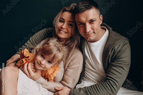 Photoshoot of a happy young family. Dad, mom and daughter. Studio photography.