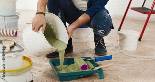 Fotografie Close up of Caucasian young handsome man pouring green olive paint preparing for painting walls in house renovating and redesigning room