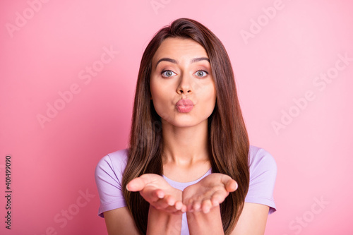 Photo portrait of girl blowing air kiss with two hands together isolated on pastel pink colored background