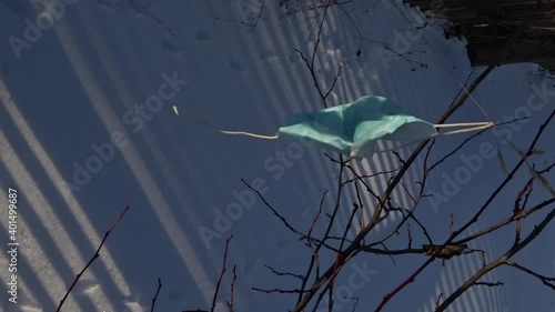 
Medical mask from covid-19 sways in wind in winter garden on sunny day