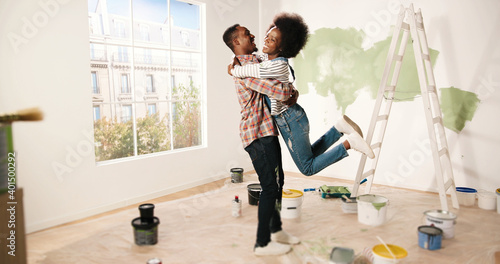 African American happy young cute couple hugging and embracing in new apartment during home repair process. Joyful family couple wife and husband in good mood renovating house. Improvement concept