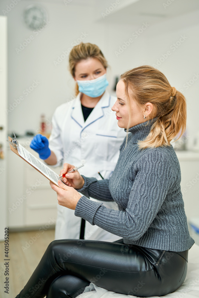 Obraz premium Mass vaccination of the population. Female doctor in a mask gives the patient documents to sign before giving her the Covid-19 antiviral vaccine