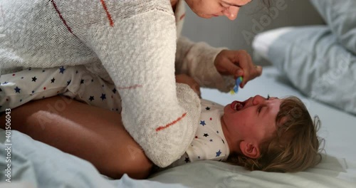 Candid mother brushing crying baby teeh. Upset infant boy not wanting to brush teeth photo