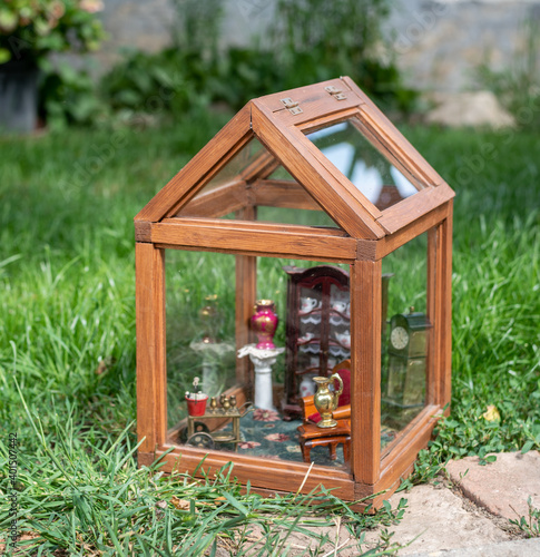 Miniature glass house outside in the grass - with small doll house furnitures: china ware cabinet, porcelain vase, chair and buffet car