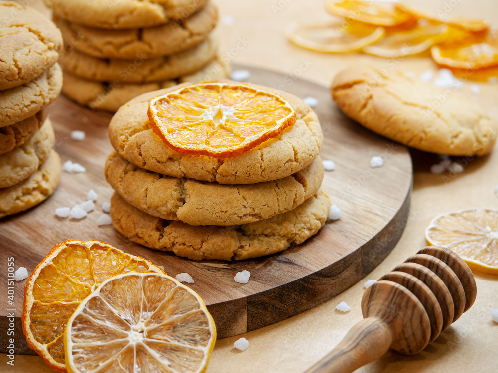 Homemade honey gingerbread cookies are stacked on a round wooden tray decorated with dried oranges, lemons, cooking sugar and a honey dipper. Horizontal. Warm tones. Close-up.