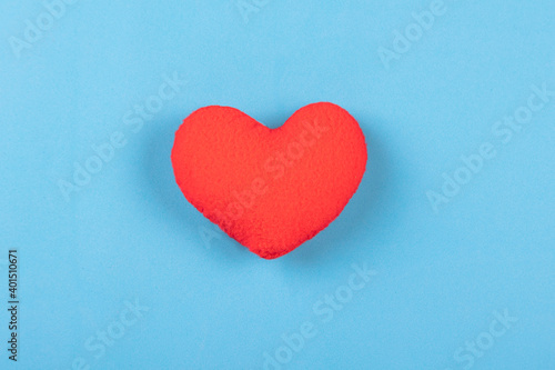 Red decorative pillow in shape of heart on blue background.