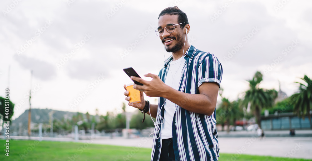 Smiling ethnic hipster messaging on smartphone in park Smiling ethnic hipster messaging on smartphone in park
