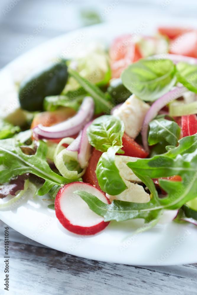 Salad with feta cheese, radish, rocket, green olives, tomatoes, cucumber and fresh basil. Bright wooden background. Close up. Salad with feta cheese, radish, rocket, green olives, tomatoes, cucumber and fresh basil. Bright wooden background. Close up.