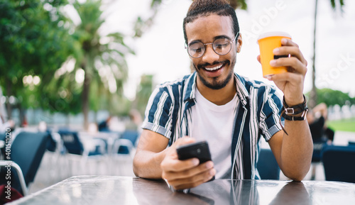 Cheerful ethnic guy browsing smartphone in street cafe