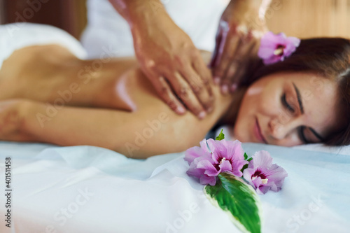 Purple flower lying down. Man does massage to the young woman in white towel indoors