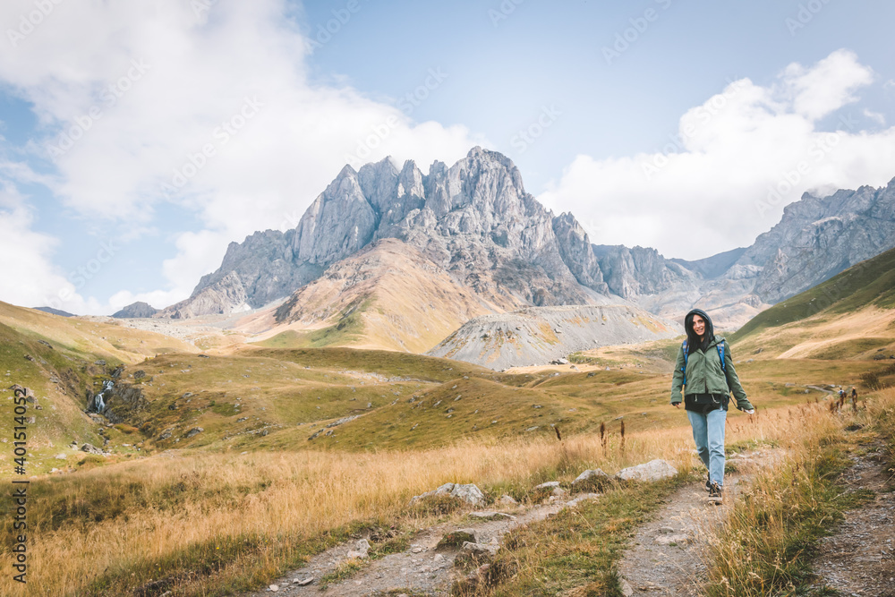 Happy female caucasian woman walks down the path in Juta valley with scenic mountain landscape. KAzbegi travel destination