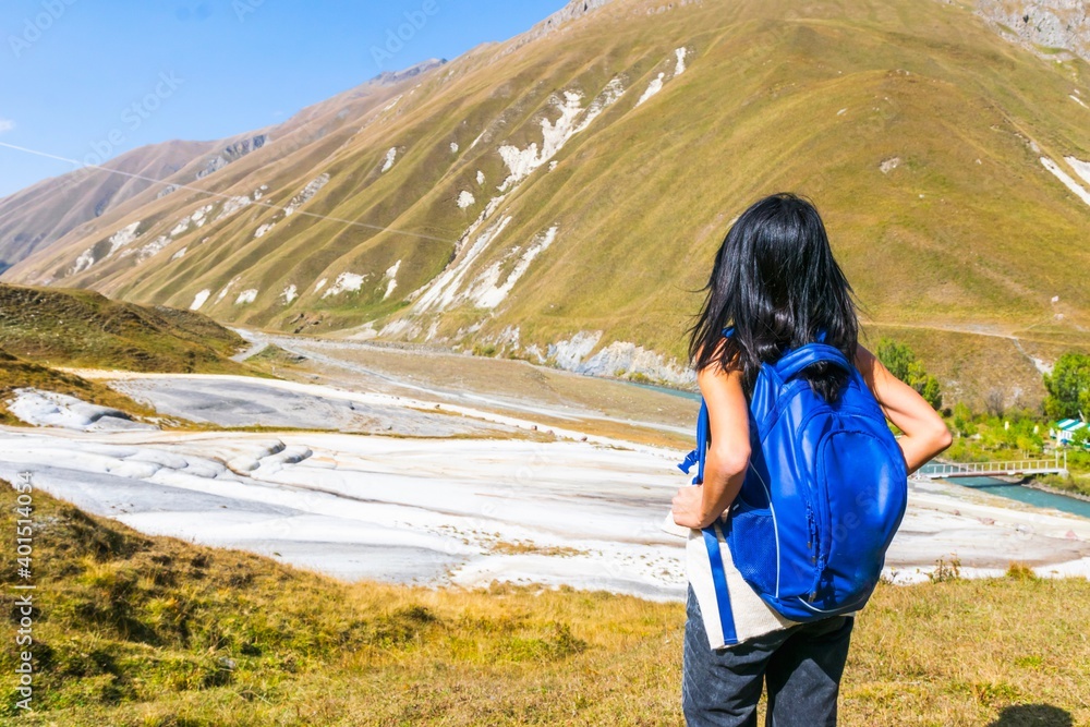 Female black hair woman with backpack stands and looks to white treventines in Truso valley. Georgia travel destination