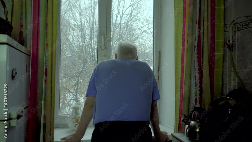 An elderly man looks out the window in the kitchen. Gradually, the fatigue of self-isolation during the pandemic begins to accumulate An elderly man looks out the window in the kitchen. Gradually, the fatigue of self-isolation during the pandemic begins to accumulate