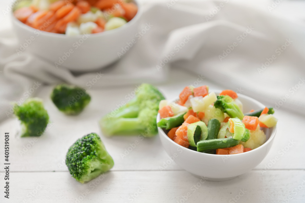 Frozen vegetables in bowls on light wooden background