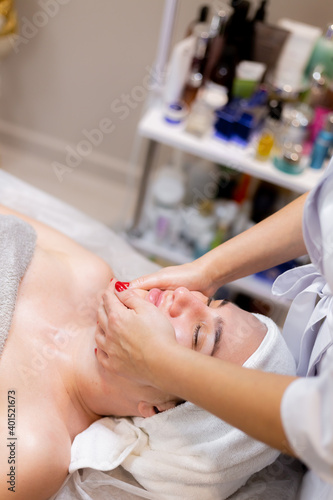 A young beautiful girl lies on the beautician s table and receives procedures  a light facial massage. Woman takes care of herself  enjoys massage
