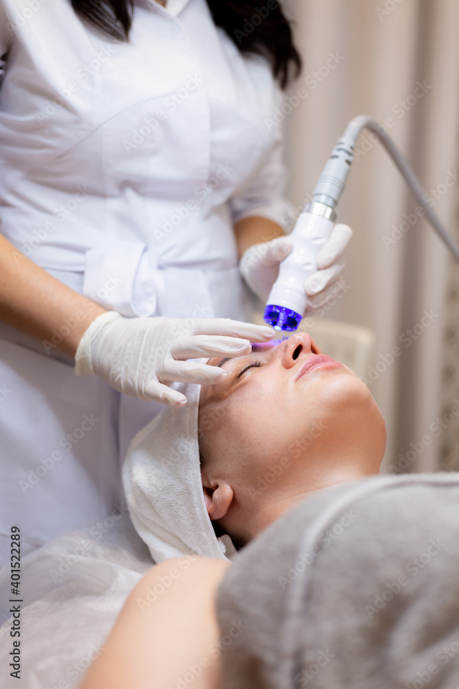 A young beautiful girl lies on the beautician's table and receives procedures with a professional apparatus for skin rejuvenation and moisturizing A young beautiful girl lies on the beautician's table and receives procedures with a professional apparatus for skin rejuvenation and moisturizing