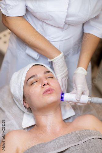 A young beautiful girl lies on the beautician's table and receives procedures with a professional apparatus for skin rejuvenation and moisturizing