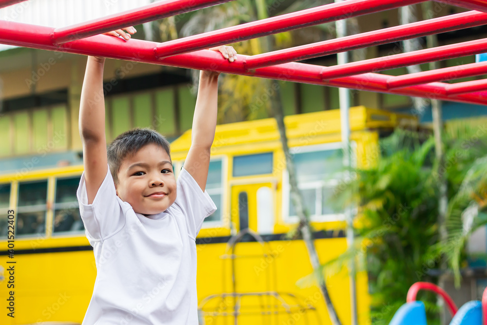 Obraz premium Kid exercise for health and sport concept. Happy Asian student​ child boy playing and hanging from a steel bar at the playground. 6-7 years old.