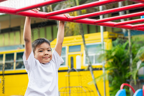 Kid exercise for health and sport concept. Happy Asian student​ child boy playing and hanging from a steel bar at the playground. 6-7 years old. © waridsara