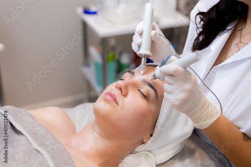 A young beautiful girl lies on the beautician s table and receives procedures with a professional apparatus for skin rejuvenation and moisturizing